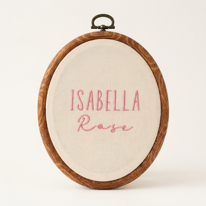Oval woodgrain frame with pink Isabella Rose name embroidery on cream fabric